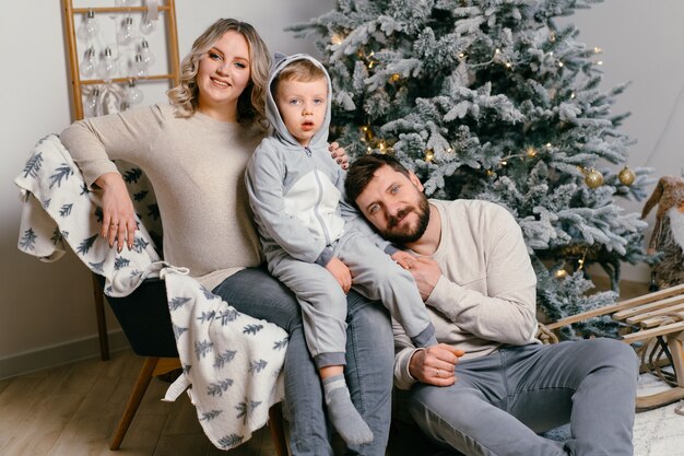 Felicità della famiglia di Natale Ritratto di papà, mamma incinta e figlio piccolo seduto sulla poltrona a casa vicino all'albero di Natale abbraccio sorriso mattina europea di vacanza in famiglia per giovani adulti