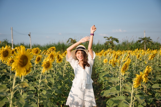 Felicità della giovane donna asiatica e alzando le braccia sul campo di girasole in campagna alla sera