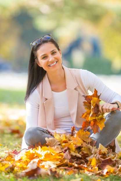 Felicità donna seduta nel parco autunnale che tiene il mazzo con foglie d'autunno.