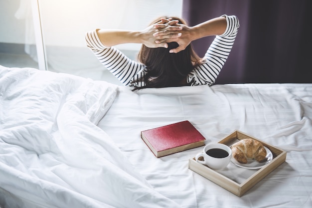 felicità donna sul letto con vecchio libro e mattina tazza di caffè e croissant