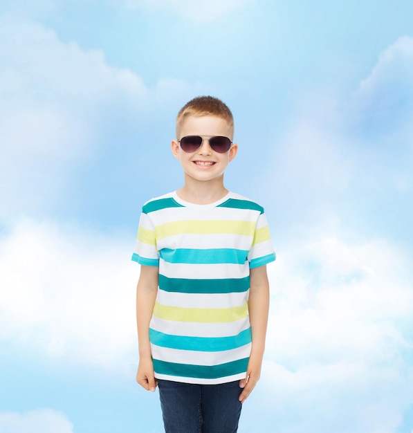 felicità, estate, infanzia e concetto di persone - ragazzino carino sorridente in occhiali da sole su sfondo blu cielo nuvoloso