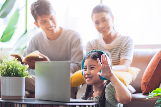 Felicità figlia asiatica indossa le cuffie studio online durante l'istruzione a casa madre e padre asiatici si divertono a guardare sul divano divano a casa casa quarantena online imparando un nuovo stile di vita normale