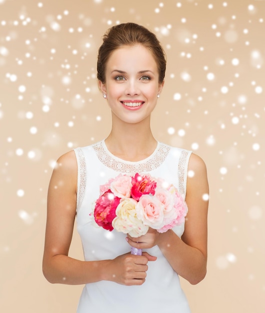 felicità, matrimonio, vacanze e concetto di celebrazione - sposa sorridente o damigella d'onore in abito bianco con bouquet di fiori su sfondo beige e neve