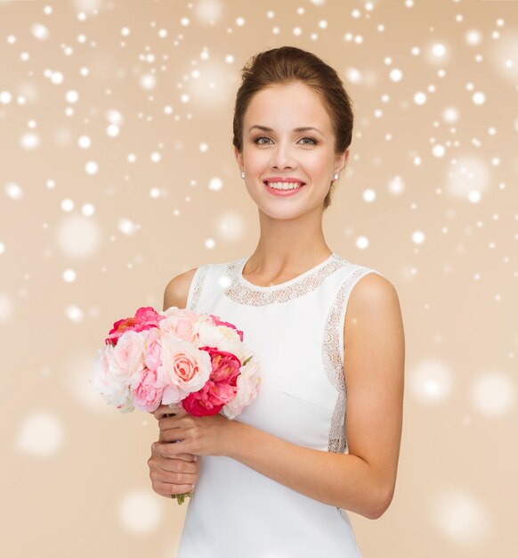 felicità, matrimonio, vacanze e concetto di celebrazione - sposa sorridente o damigella d'onore in abito bianco con bouquet di fiori su sfondo beige e neve