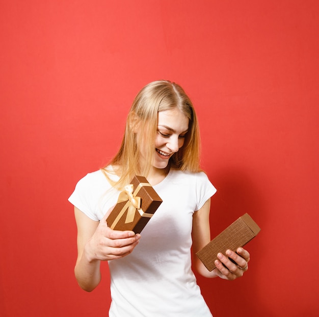Felicità sul volto di una ragazza bionda con un regalo in mano su uno sfondo rosso