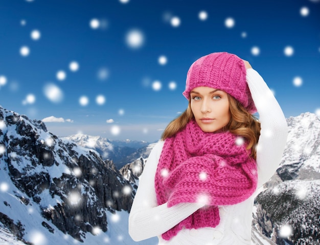 felicità, vacanze invernali, natale e concetto di persone - giovane donna con cappello rosa e sciarpa su sfondo di montagne innevate