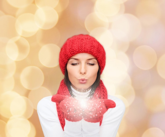 felicità, vacanze invernali, natale e concetto di persone - giovane donna sorridente con cappello rosso, sciarpa e guanti su sfondo di luci beige