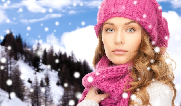 felicità, vacanze invernali, natale e concetto di persone - primo piano di giovane donna con cappello rosa e sciarpa su sfondo di montagne innevate