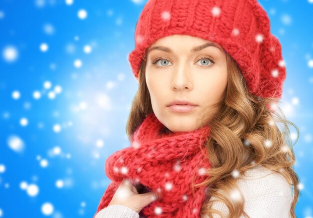 felicità, vacanze invernali, natale e concetto di persone - primo piano di giovane donna con cappello rosso e sciarpa su sfondo blu innevato
