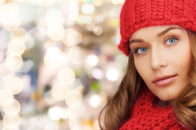 felicità, vacanze invernali, natale e concetto di persone - primo piano di una giovane donna sorridente con cappello rosso e sciarpa su sfondo di luci