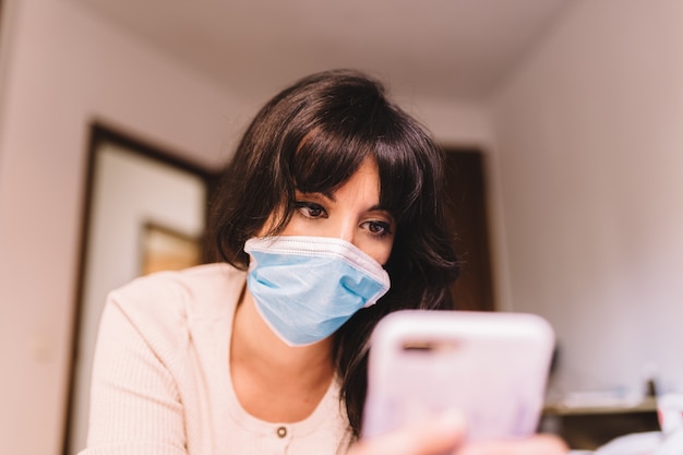 Femmina a casa nel respirare maschera respiratoria medica sul viso con il cellulare. coronavirus pandemico, virus covid-19. Quarantena, prevenire il concetto di infezione. Concentrati sul suo viso.