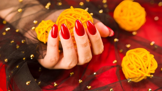 Femmina anonima con manicure rossa con palline di vimini decorative su sfondo rosso
