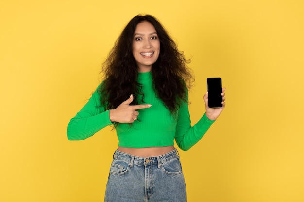 Femmina araba felice che mostra lo schermo vuoto del cellulare sopra fondo giallo