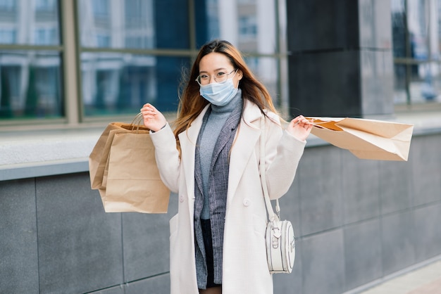 Femmina asiatica in un cappotto, occhiali e una maschera medica si trova sulla strada, con in mano un pacchetto.