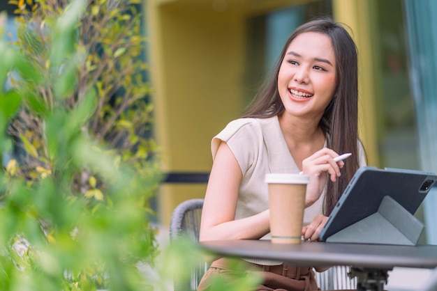 Femmina asiatica nomade digitale felicità libertà sorridente allegro lavorando utilizzando tablet in giardino outdoorasia donna freelance relax tempo libero lavorando ovunque lavoro e viaggio iwith giardino bokeh sfondo