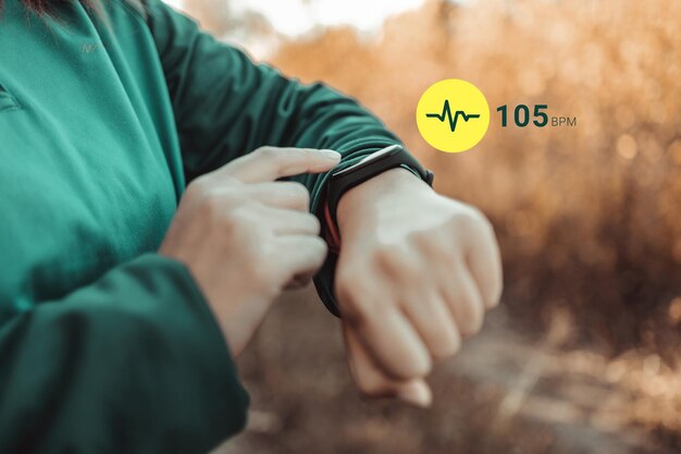 Femmina atletica che utilizza un fitness tracker o un orologio intelligente tra l'allenamento della corsa all'aperto, controllando lo sfondo del banner della frequenza cardiaca