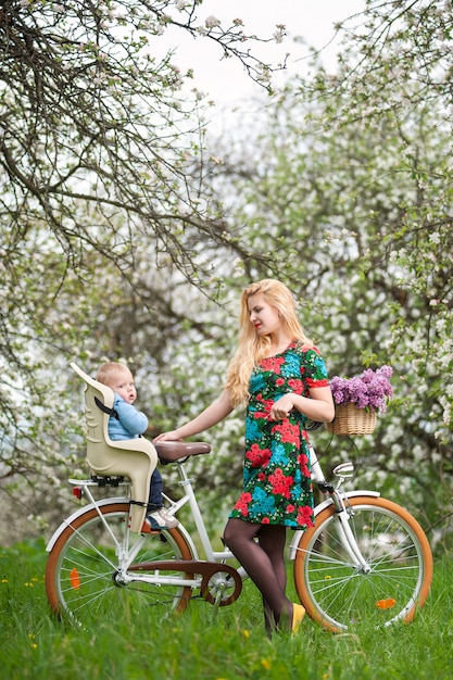 Femmina bionda con la bicicletta della città con il bambino nella sedia della bicicletta