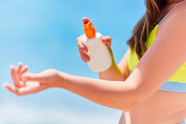 Femmina che applica e tiene una bottiglia vuota bianca vuota di crema solare mentre si prende il sole sulla spiaggia in riva al mare nella soleggiata giornata estiva Protezione solare
