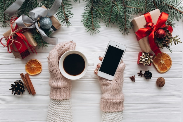 Femmina che tiene caffè tazza, smartphone e confezionamento regali di Natale.