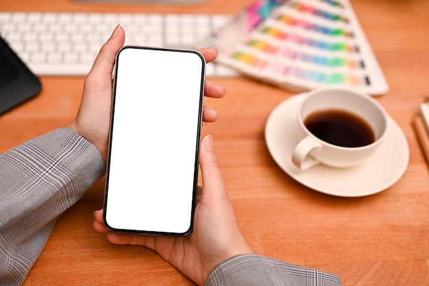 Femmina che tiene un mockup di smartphone sopra la scrivania dell'ufficio del designer grafico moderno