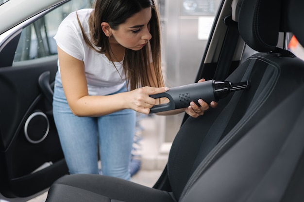 Femmina che utilizza un aspirapolvere portatile nella sua auto aspirapolvere elettrico nella macchina pulita a mano della donna all'interno