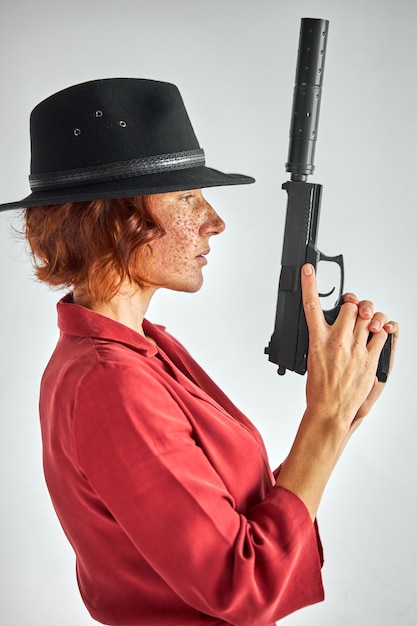 femmina con arma contro bianco ,. donna rossa detective in cerca cappello nero