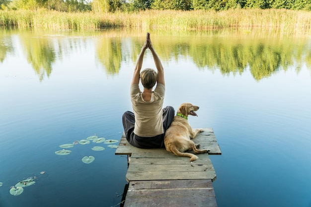 Femmina con un cane labrador su un ponte di pesca in legno che si esercita e si gode una tranquilla vista sull'acqua calda Relax e tempo libero con animali domestici domestici