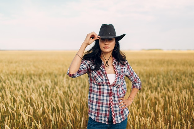 Femmina contadina americana con cappello da cowboy, camicia a quadri e jeans sul campo di grano