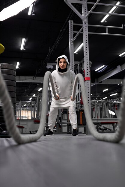 Femmina cross fit atleta musulmano in hijab lavorando con corde pesanti cercando determinad e concentrato di allenamento funzionale atletica fitness attività sportiva rafforzamento della fiducia