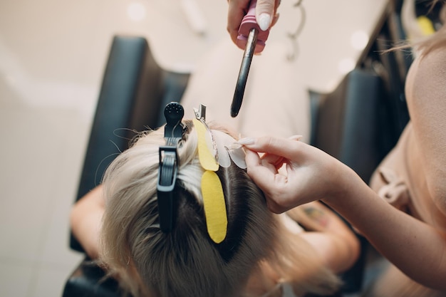 Femmina di parrucchiere che fa le estensioni dei capelli alla giovane donna con capelli biondi nell'estensione professionale dei capelli del salone di bellezza