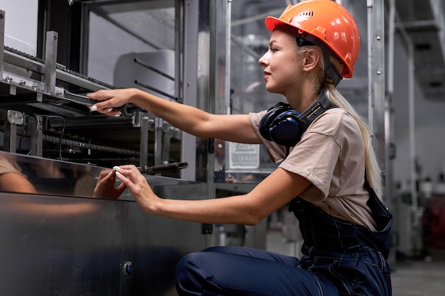 Femmina esperta che ripara apparecchiature rotte in fabbrica usando una chiave inglese, in uniforme