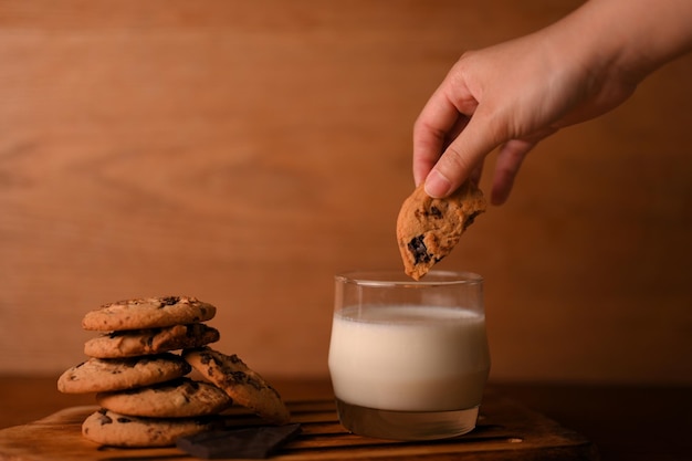 Femmina immergendo un pezzo di biscotto al cioccolato di arachidi in un bicchiere di latte Yummy concetto di colazione