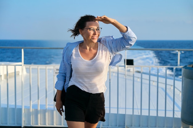 Femmina in camicia blu sul ponte della nave guardando lo sfondo del tramonto del mare del cielo di vista sul mare