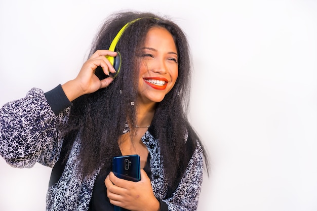 Femmina ispanica che ascolta la musica con le cuffie sul muro bianco