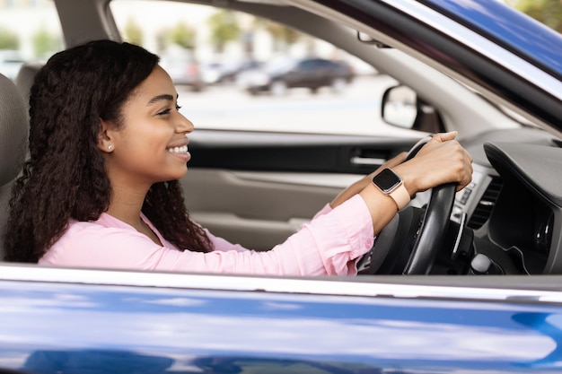 Femmina nera sorridente che guida la nuova automobile in città