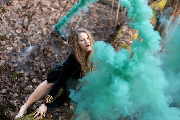 Femmina sciamano che tiene in mano una bomba a fumo verde sul tronco dell'albero