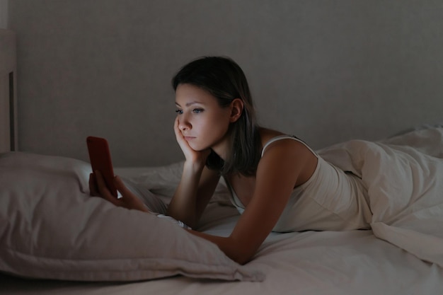 Femmina sdraiata a letto e guardando il suo smartphone di notte