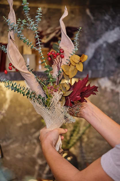 Femmina senza volto che dimostra un bouquet di fiori secchi, bacche e rami di eucalipto in un negozio di fiori