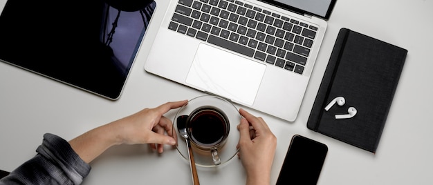 Femmina su semplice area di lavoro, tenendo la tazza di caffè e guardando sul laptop mock-up