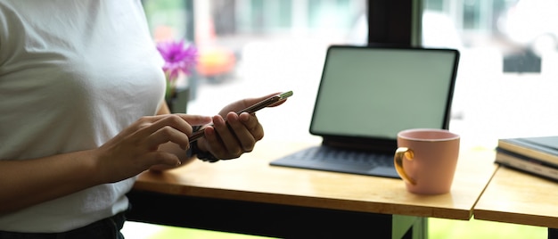 Femmina utilizza lo smartphone mentre è seduto al tavolo da lavoro con mock up tablet