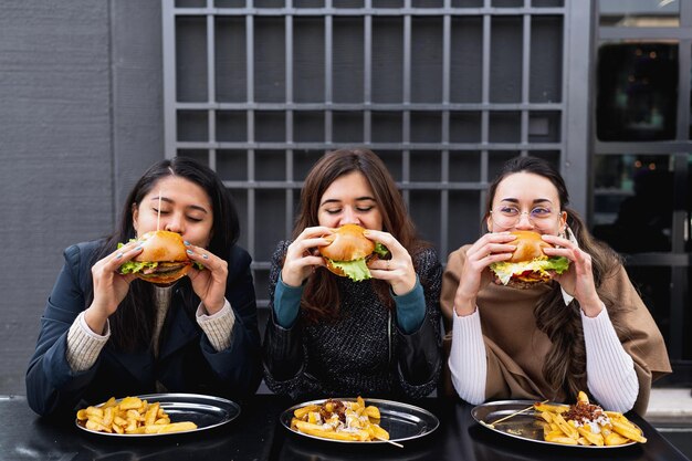 Femmine sedute al tavolo del ristorante che mordono hamburger. Fast food mangiare malsano.