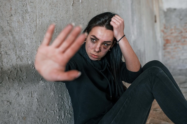 Ferma la violenza Giovane donna picchiata in abiti neri seduta sul pavimento di un edificio abbandonato