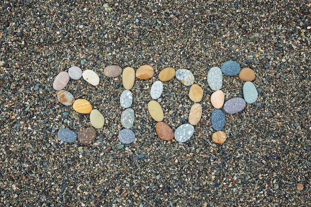 Fermata di testo fatta di pietre sulla spiaggia sabbiosa