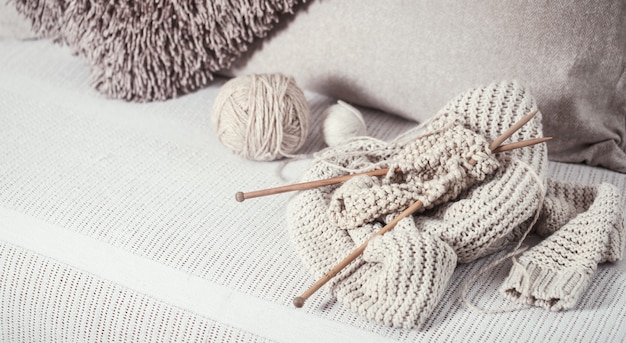 Ferri da maglia vintage in legno e fili per lavorare a maglia su un accogliente divano con cuscini e maglioni