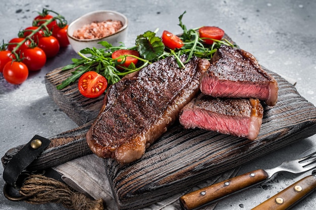 Fesa di berretto arrosto o bistecca di carne di manzo controfiletto superiore su tavola di legno con insalata. Sfondo grigio. Vista dall'alto.