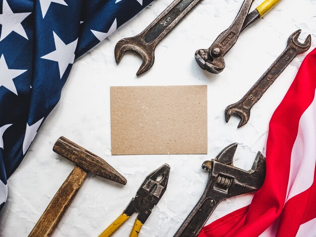 FESTA DEI LAVORATORI. Utensili manuali e la bandiera degli Stati Uniti d'America sdraiati sul tavolo. Vista dall'alto, primo piano. Congratulazioni a familiari, parenti, amici e colleghi. Concetto di festa nazionale