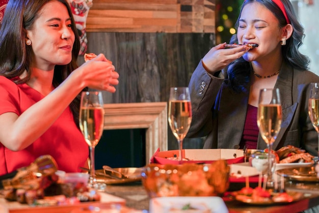 Festa della bella donna asiatica amica che celebra. donne che mangiano pizza sul tavolo con snack e bevande. felicità amici vigilia di natale celebrazione cena cibo e champagne.