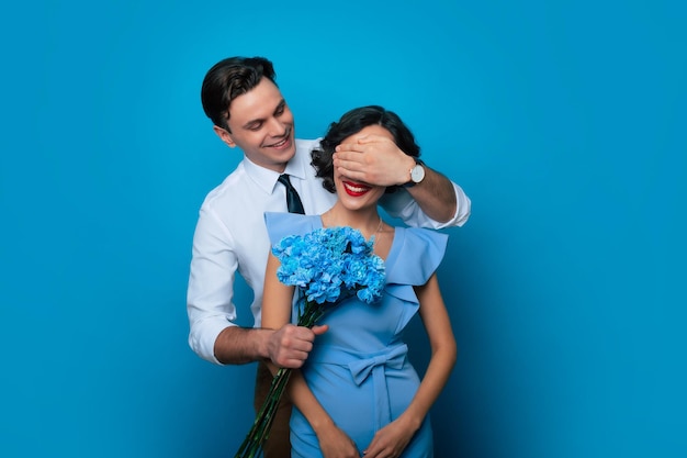 Festa della donna San Valentino Compleanno Vacanze presenta Sorridente bell'uomo sta regalando un bouquet di fiori blu per la sua ragazza piuttosto elegante mentre si copriva gli occhi