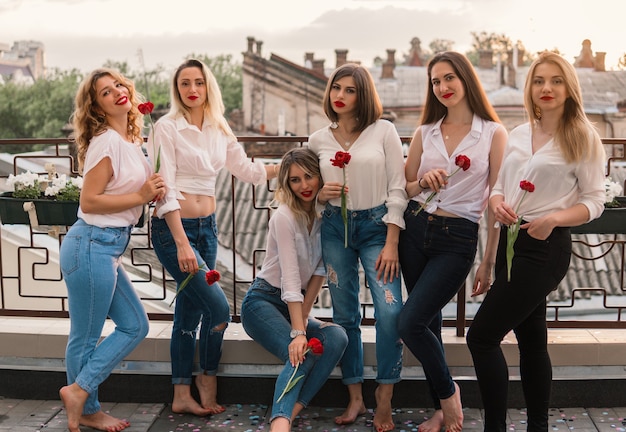 Festa delle ragazze. Belle donne amiche sul balcone o sul tetto con fiori alla festa di addio al nubilato. Indossano gli stessi vestiti