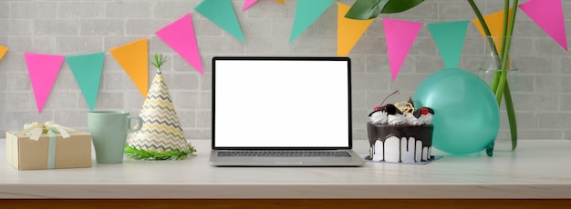 Festa di compleanno online con laptop schermo vuoto, torta, cappello da festa e decorazioni